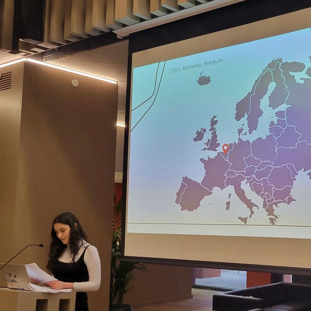 Sofia Weingarten delivers presentation on Holocaust Remembrance Day, she stands at a podium in front of projected image of map of Europe